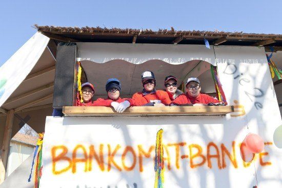 Fünf Personen in roten Uniformen und Mützen posieren für ein Foto aus einem Fenster einer dekorierten Struktur mit Graffiti und Luftballons.