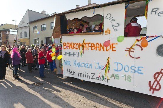 Ein festlicher Umzug mit einem geschmückten Wagen, bunten Graffiti, Luftballons und Zuschauern auf der Straße.