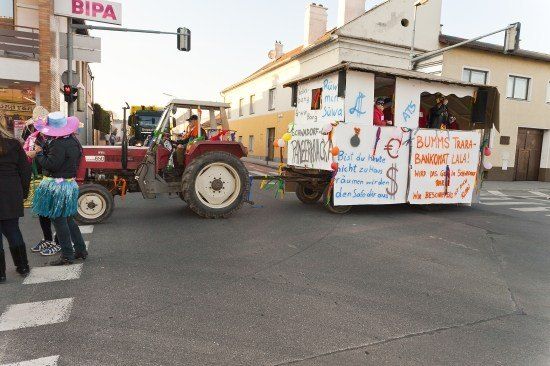 Ein Traktor mit einem Anhänger, der mit Luftballons und Schildern verziert ist, fährt mit Zuschauern auf der Straße.