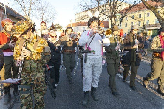Eine Gruppe von Menschen in verschiedenen Kostümen, einschließlich Militäruniformen, marschiert in einem Umzug und spielt Musikinstrumente.