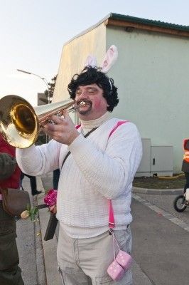 Ein Mann in einem weißen Pullover und Hasenohren spielt eine Trompete im Freien.