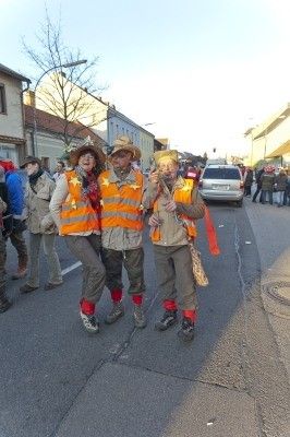 Drei Personen in reflektierenden Westen und Hüten posieren für ein Foto auf einer Straße während eines Umzugs.