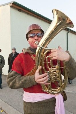 Ein Mann in einem roten Shirt und einem Helm spielt Tuba auf einer Straße.