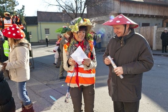 Eine Frau in einem Blumenhut hält ein Papier, während ein Mann mit einem Pilzhut neben ihr lächelt auf der Straße.