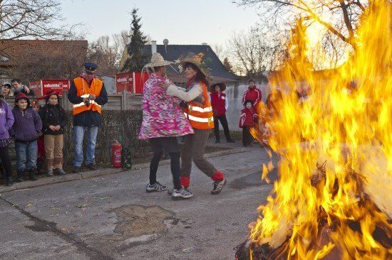 Zwei Frauen tanzen vor einem Lagerfeuer, während Menschen vom Bürgersteig zusehen.