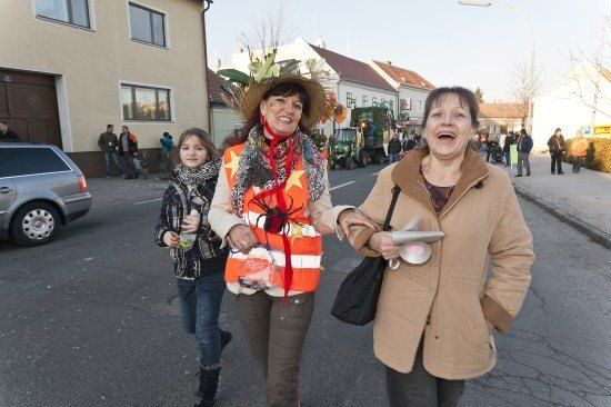Drei Frauen gehen während einer Parade auf einer Straße, eine trägt einen Hut mit Blumen und einer Spinne.