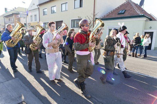 Eine Gruppe von Musikern in verschiedenen Kostümen marschiert die Straße entlang und spielt Blechblasinstrumente.