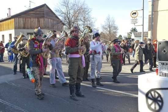 Eine Blechbläsergruppe in bunten Kostümen und Stiefeln spielt auf einer Straße vor Zuschauern.