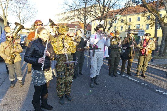 Eine Gruppe von Menschen in Militäruniformen und Mützen steht auf der Straße und spielt Musikinstrumente.
