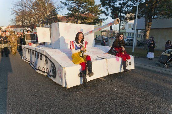 Zwei Frauen, die als Schneewittchen verkleidet sind, sitzen auf einem Panzerwagen während einer Parade, mit einer Menge und Gebäuden im Hintergrund.