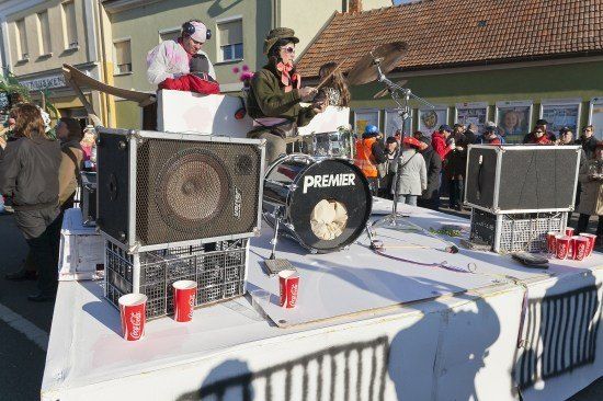 Eine Straßenaufführung mit einem Schlagzeuger und einem Gitarristen auf einer Bühne mit Lautsprechern und Bechern, umgeben von einer Menge.