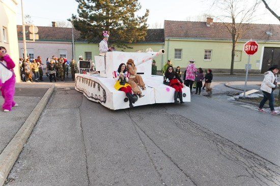 Ein Paradewagen in Form eines Panzers mit Menschen in Kostümen, die darauf reiten, während eine Menge auf dem Bürgersteig zuschaut.
