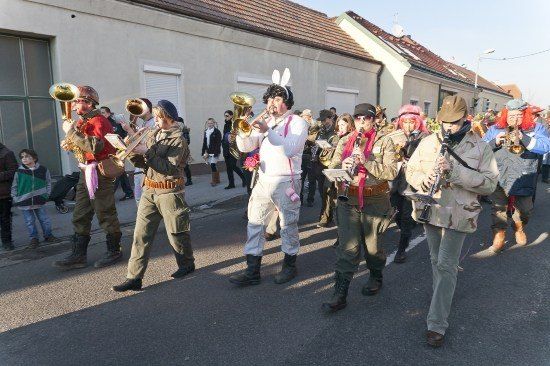 Eine Gruppe von Menschen in verschiedenen Kostümen, darunter Hasenohren und Militäruniformen, marschiert bei einer Parade und spielt Musikinstrumente.