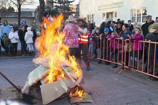 Eine Menschenmenge beobachtet, wie ein Lagerfeuer in der Mitte der Straße brennt, mit zwei Personen in der Nähe.