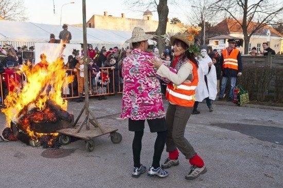 Zwei Frauen tanzen in der Nähe eines Lagerfeuers, umgeben von einer Menge Menschen in festlicher Kleidung.