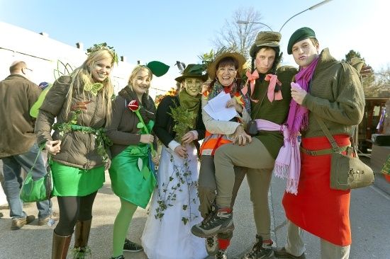 Eine Gruppe von Menschen in grünen Kostümen posiert für ein Foto im Freien. Sie halten Pflanzen und Blumen.
