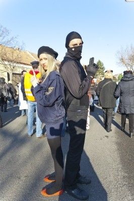 Eine Frau und ein Mann in schwarzen Kostümen und Masken stehen zusammen in einer Menschenmenge auf einer Straße.