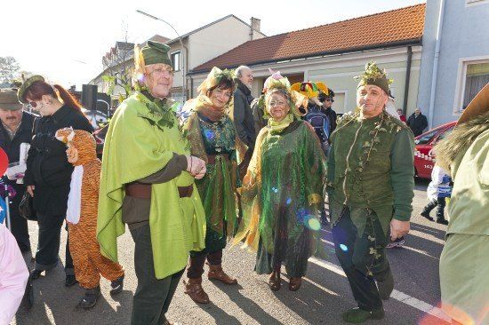 Eine Gruppe von Menschen in grünen Kostümen mit Blättern und Blumen steht auf einer Straße, möglicherweise während eines Umzugs.
