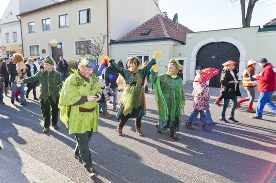 Eine Gruppe von Menschen in grünen Kostümen und Hüten zieht bei einem Umzug auf einer Straße.