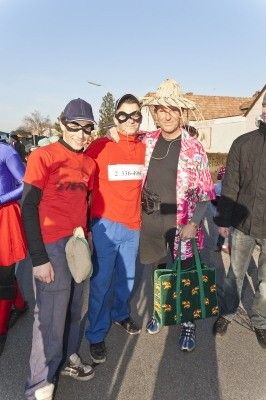 Vier Menschen in Kostümen stehen auf einer Straße, einer hält eine grüne Tasche und ein anderer trägt einen Strohhut.