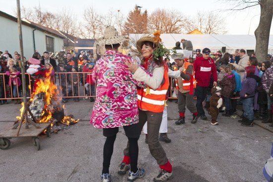 Zwei Frauen tanzen vor einem Lagerfeuer, während eine Menge zuschaut, einige tragen Hüte und Sicherheitswesten.