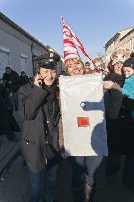 Zwei Frauen in Kostümen, eine als Polizistin gekleidet und die andere in einem rot-weißen Hut, stehen auf einer Straße mit einer Menschenmenge im Hintergrund.