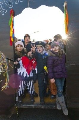 Eine Gruppe von Kindern in Kostümen, einige mit Requisiten, stehen in einem dekorierten Fahrzeug, möglicherweise für eine Parade, mit Sonnenlicht, das die Szene beleuchtet.