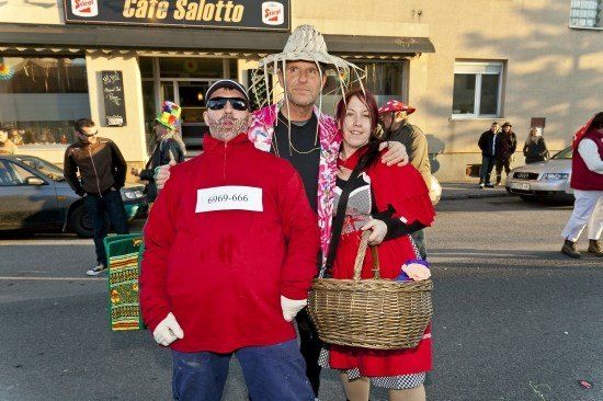 Drei Personen in roten Kostümen stehen auf einer Straße, eine hält einen Korb, mit einem Gebäude namens Cafe Salotto im Hintergrund.