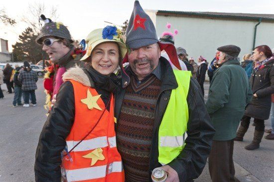 Ein Mann und eine Frau in Warnwesten stehen in einer Menschenmenge und lächeln für die Kamera. Sie sind von Menschen in Kostümen umgeben.