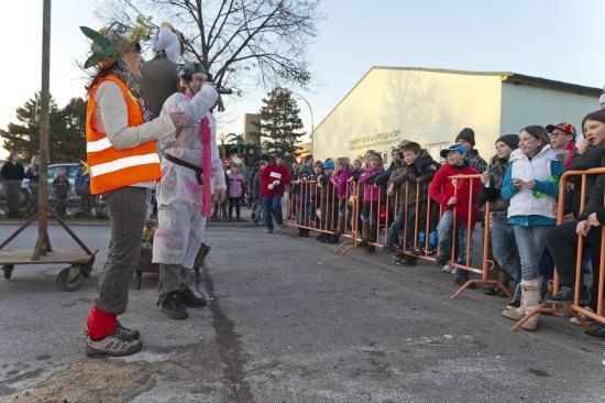 Eine Gruppe von Menschen in Kostümen führt vor einer Menge von Kindern auf, die hinter einer Metallbarriere zuschauen.