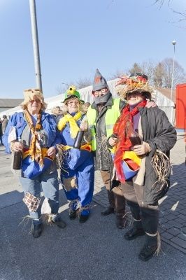 Fünf Menschen in bunten Kostümen stehen zusammen auf einem gepflasterten Weg. Sie alle lächeln und scheinen für ein Foto zu posieren.