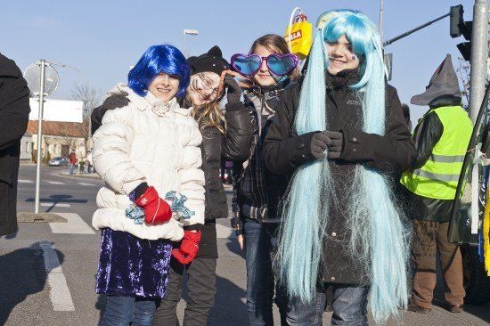 Vier junge Frauen in Kostümen, zwei mit blauen Perücken, eine mit einer Katzenohr-Mütze und eine mit herzförmigen Gläsern, stehen auf einer Straße.