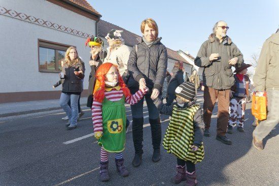 Eine Gruppe von Menschen, darunter zwei Kinder in Kostümen, gehen auf einer Straße vor einem Gebäude.