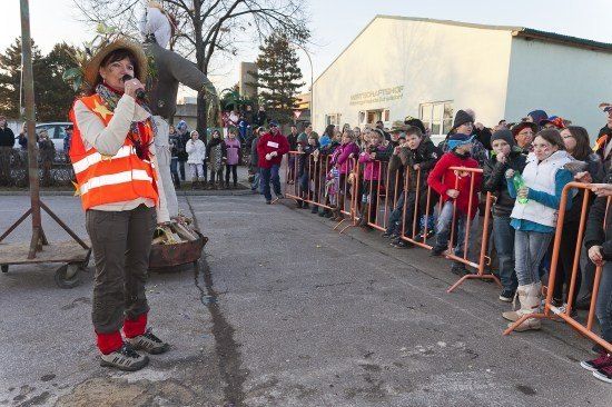 Eine Frau in einer Warnweste und Hut steht vor einer Menge und hält ein Mikrofon. Die Menge steht hinter orangefarbenen Barrieren.