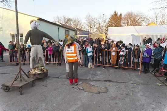 Eine Menschenmenge in Kostümen, darunter eine Person in einer Kürbis-Kostüm, beobachtet, wie eine Person in einer orangefarbenen Weste neben einem Schubkarren mit einem Feuerkorb steht.
