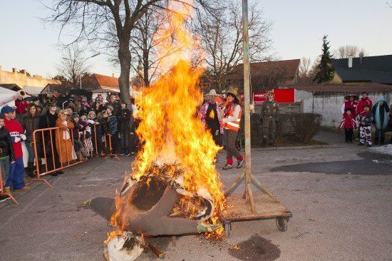 Ein großes Lagerfeuer brennt in der Mitte einer Straße, umgeben von einer Menschenmenge. Einige tragen Hüte und Schuhe.