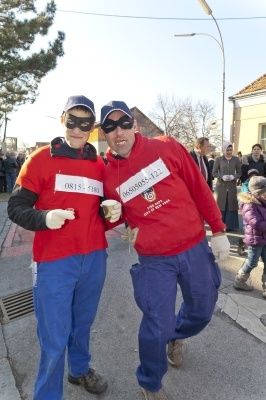 Zwei Männer in roten und blauen Kostümen, mit Masken, gehen auf einer Straße, mit einer Menge im Hintergrund.