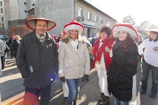 Eine Gruppe von Menschen in Winterkleidung, einschließlich Hüten, geht auf einer Straße mit Gebäuden und Bäumen im Hintergrund.