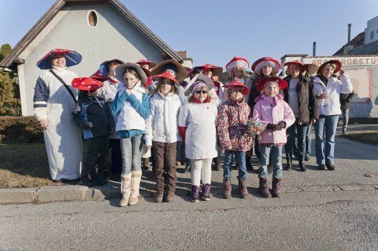 Eine Gruppe von Kindern und Erwachsenen, alle mit roten Hüten, stehen an einem sonnigen Tag in einer Reihe vor einem Gebäude.