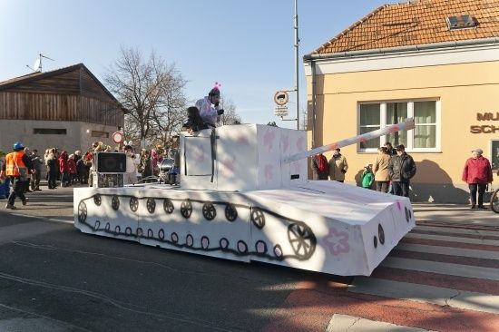 Ein Panzer-förmiger Wagen steht auf der Straße mit Menschen um ihn herum. Ein Mann steht auf dem Panzer.