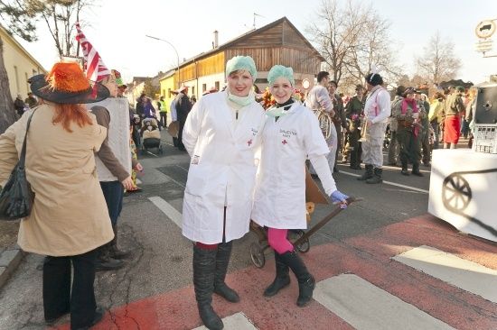 Zwei Frauen in weißen Laborkittel und Haarnetzen stehen auf einer Straße mit einer Menschenmenge im Hintergrund.