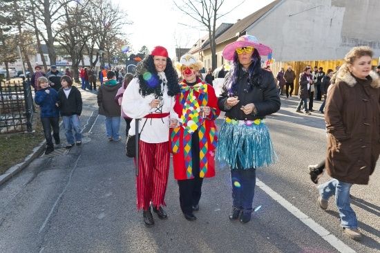 Drei Menschen in Kostümen gehen während eines Umzugs mit Zuschauern im Hintergrund die Straße entlang.