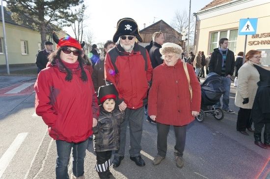 Eine Gruppe von Menschen in roten Kleidungsstücken steht auf der Straße, möglicherweise für eine Parade. Ein Mann in einem Piratenhut und eine Frau in einer roten Mütze sind unter ihnen.