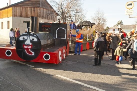 Ein dekorierter Zugwagen mit einem aufgemalten Gesicht steht auf der Straße, umringt von Menschen.