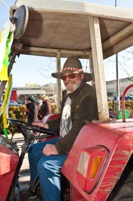 Ein älterer Mann mit Hut und Sonnenbrille sitzt in einem roten Traktor, möglicherweise für ein Foto.