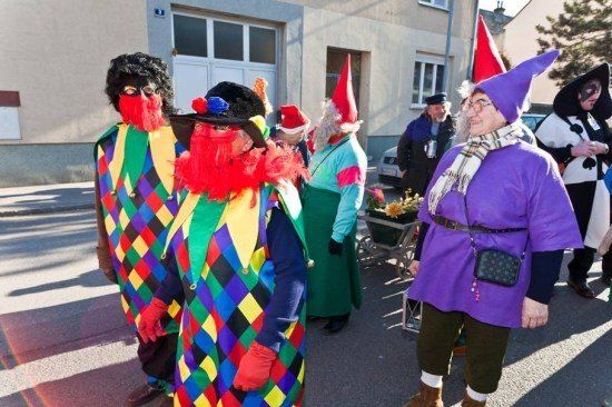 Eine Gruppe von Menschen in bunten Kostümen, darunter ein Narr, steht auf einer Straße.