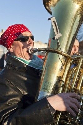 Ein Mann mit rotem Bandana und Sonnenbrille spielt Tuba bei einer Veranstaltung im Freien.