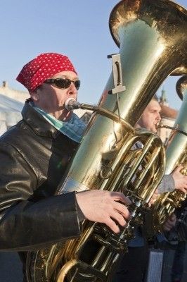 Ein Mann mit rotem Kopftuch und Sonnenbrille spielt Tuba, während ein anderer Musiker im Hintergrund Trompete spielt.
