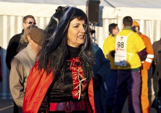 Eine Frau in einem roten und schwarzen Kostüm mit einer schwarzen Perücke steht inmitten einer Menschenmenge, von denen einige nummerierte Trikots tragen.