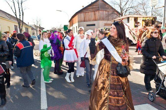 Eine Gruppe von Menschen in Kostümen, darunter eine Frau in einem braunen Kleid, geht bei einer Parade auf einer Straße.